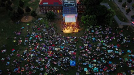 Viele Gäste sitzen auf Picknickdecken und schauen beim Südstadt Klassik Open Air zur beleuchteten Bühne mit Orchester.