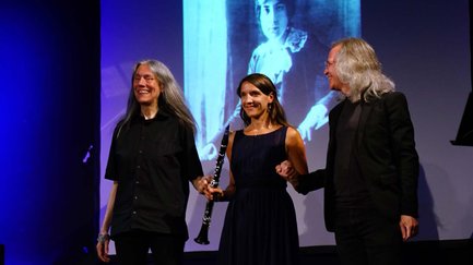 Drei Künstler halten sich nach ihrem Auftritt auf der Bühne vor der Projektion einer jungen Komponistin.