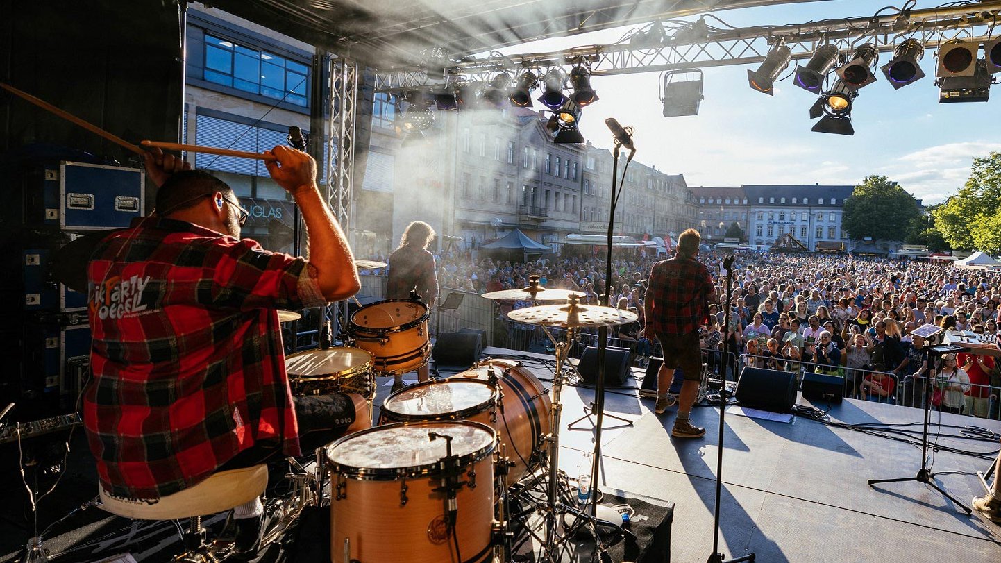 Blick von der Bühne auf das Publikum beim Fürth Festival, Band spielt mit Schlagzeug, Keyboard, Gitarre und Gesang