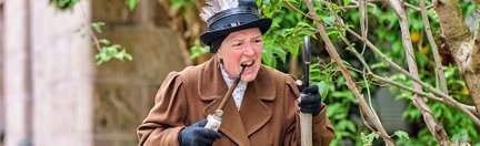 Ältere Frau im Mantel und Federnhut hält Pfeife und Regenschirm – bekannt als Fürther Pfeifndurla.