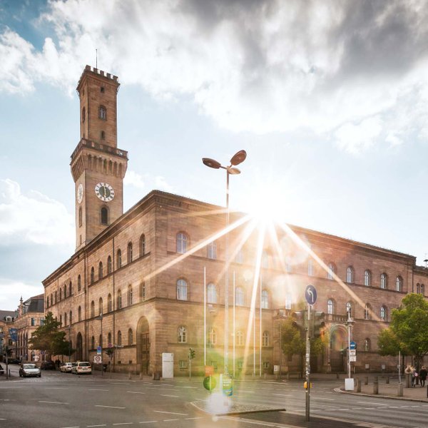 Das Fürther Rathaus mit majestätischem Turm, hinter dem die Sonne hell hervorscheint.