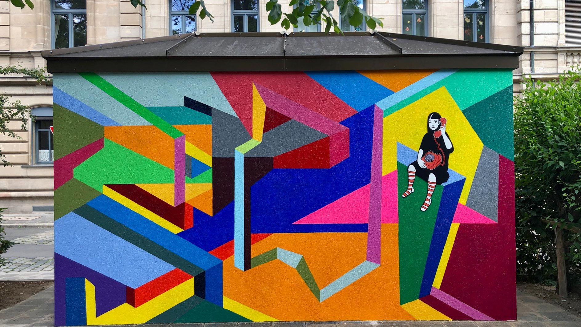 Farbige geometrische Wandmalerei mit einer stilisierten Mädchenfigur, die einen roten Telefonhörer hält.