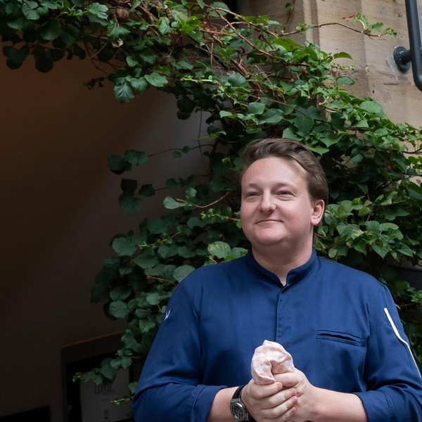 Tim steht vor dem eleganten Eingang des Werners Boutique Hotels, einem Sandsteingebäude mit grünen Pflanzen.