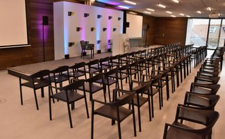 Großer Veranstaltungsraum mit Stuhlreihen, Bühne, Rednerpult, Ludwig Erhard Figur, Leinwände und Fensterfront