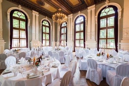Saal im Logenhaus Fürth mit rund gedeckten weißen Tischen, Kerzen, Stuhlhussen, großen Fenstern und Kronleuchtern