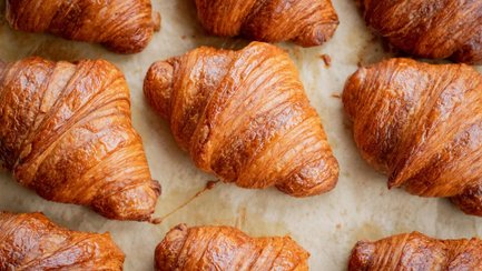 Mehrere frisch gebackene, goldbraune Croissants liegen dicht nebeneinander auf einem Backpapier.