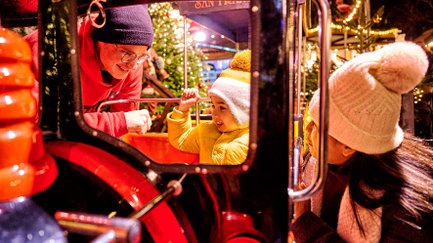 Kleiner Junge im Kinderzug, während seine Eltern daneben knien und den festlichen Weihnachtsmarkt genießen.