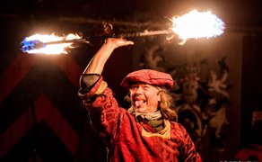 Gaukler in rotem Gewand zeigt Feuershow auf dem Fürther Mittelaltermarkt und schwingt einen brennenden Stab.