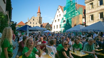 Besucher sitzen auf Bierbänken am Grünen Markt und schauen in Richtung Bühne der Veranstaltung.
