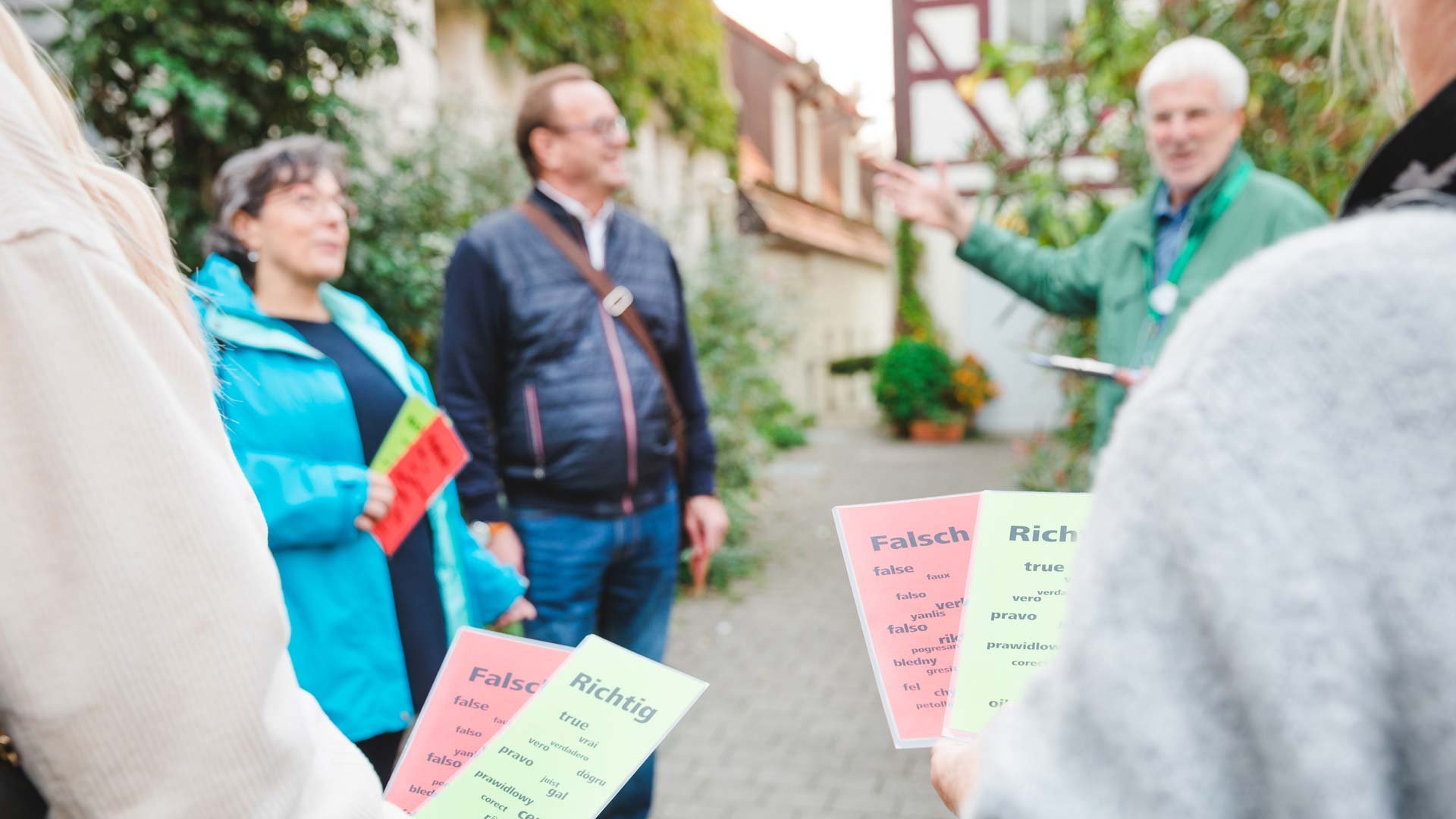 Teilnehmer einer Stadtführung halten rote und grüne Karten mit "Falsch" und "Richtig", während sie dem Stadtführer zuhören.