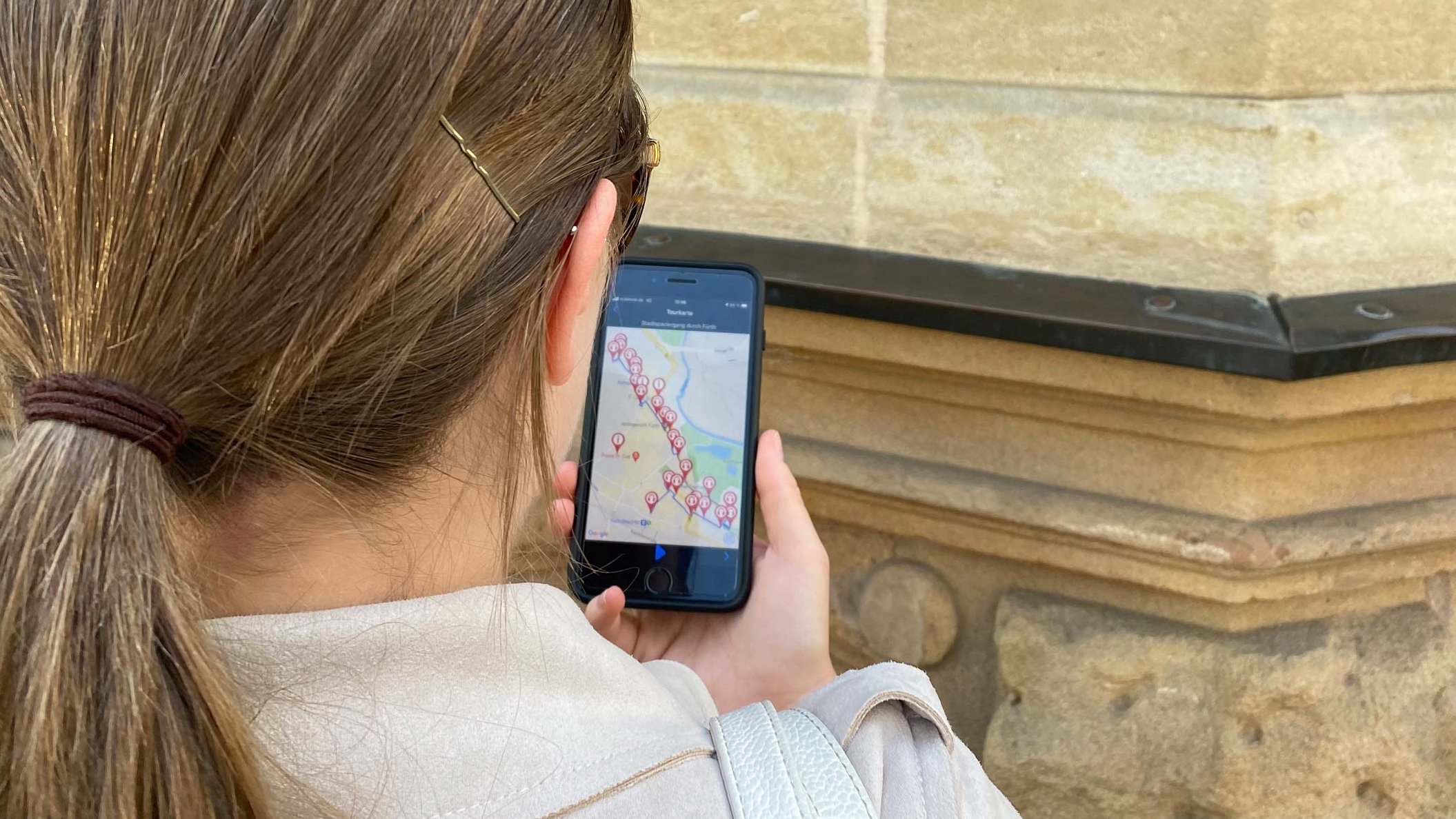 Frau blickt auf Handy mit Stadtkarte, im Vordergrund Sandsteinfassade und blaues Straßenschild Königswarterstraße