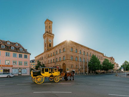 Historische Postkutsche fährt vor dem imposanten Rathaus über eine zentrale Kreuzung