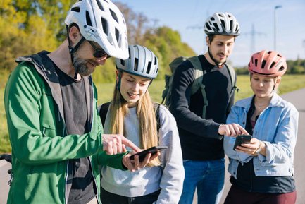 Vier Personen mit Fahrradhelmen stehen im Freien und nutzen gemeinsam Smartphones zur Orientierung.