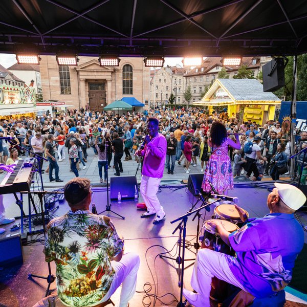 Band spielt auf dem Hallplatz, Besucher tanzen und feiern neben Essens- und Getränkeständen.