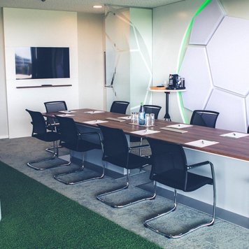 Konferenzraum mit langem Holztisch, schwarzen Stühlen, Flipchart und Fußballwanddeko