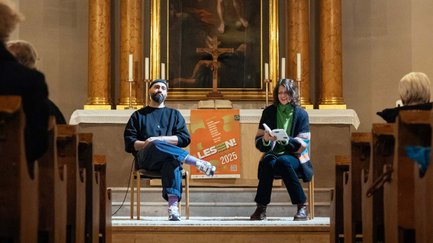 Zwei Personen am Altar der Auferstehungskirche Fürth, eine liest aus einem Buch, prunkvoller Innenraum sichtbar