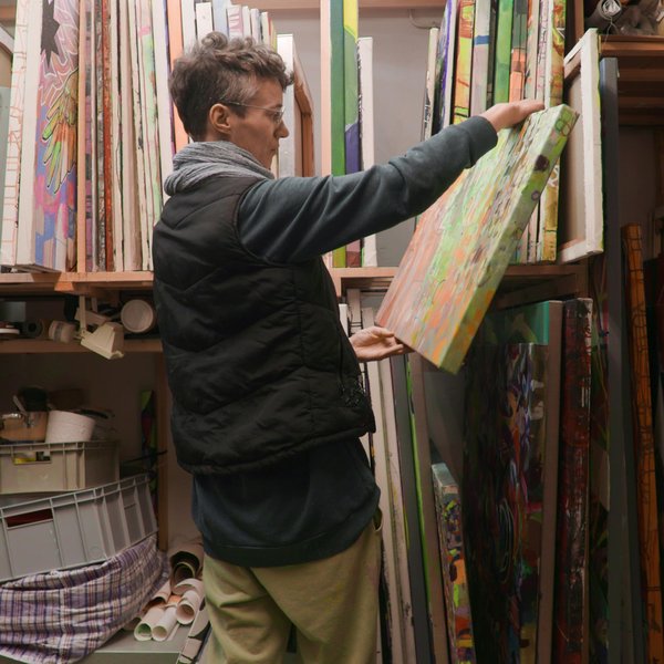 Künstlerin Sascha Bank inspiziert ein Gemälde vor einer Sammlung von Leinwänden.