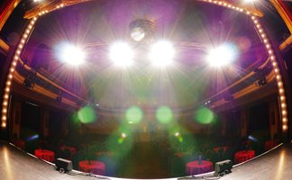 Blick von der Bühne der Comödie Fürth in den beleuchteten Saal mit Tischen und Stühlen