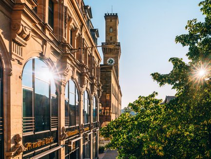 Sonnenlicht spiegelt sich im Fenster des Kaufhaus Tietz vor der Sandsteinfassade des Rathauses