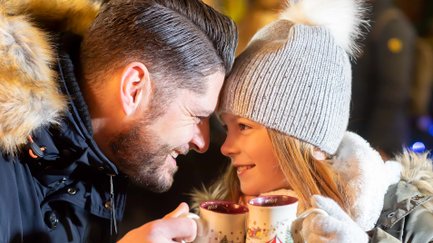 Vater und Tochter sitzen eng beisammen, lachen sich an und stoßen mit ihren Weihnachtstassen an.
