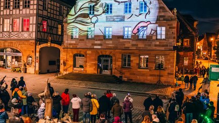 Historisches Haus am Grünen Markt in Fürth bei Glanzlichter, farbig beleuchtet, Besucher bestaunen Lichtkunst.