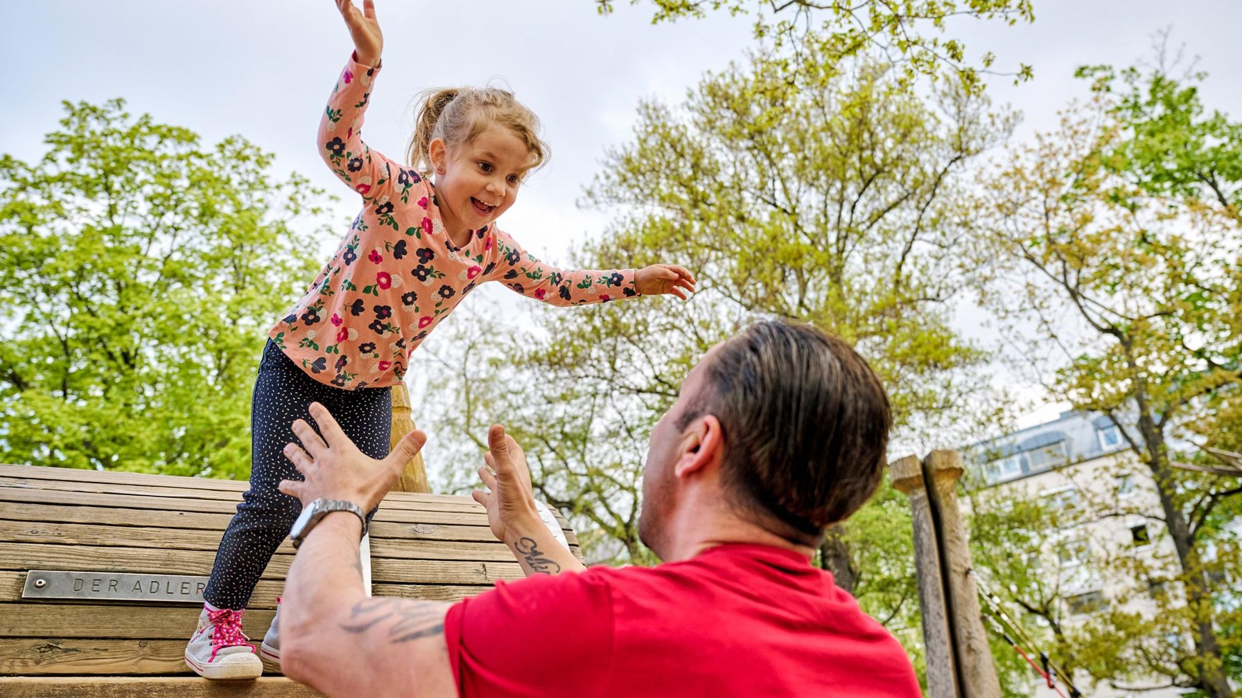 Auf dem Spielplatz in der Dr.-Konrad-Adenauer-Anlage springt ein Mädchen in die Arme ihres Papas.