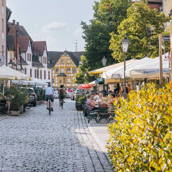 Belebte Kopfsteinpflasterstraße mit historischen Fachwerkhäusern und Außengastronomie im Sommer.
