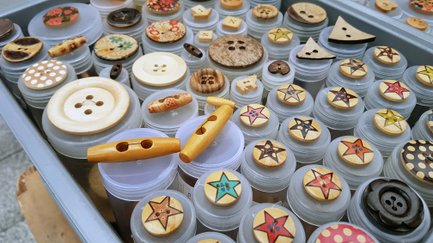 Verschiedene Knöpfe in Größe, Form und Design werden sortiert auf dem Stoffmarkt präsentiert.