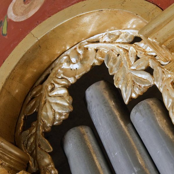 Nahaufnahme einer Orgel mit silbernen Pfeifen, goldenen Blätterranken und farbig bemalten Pflanzenmotiven.