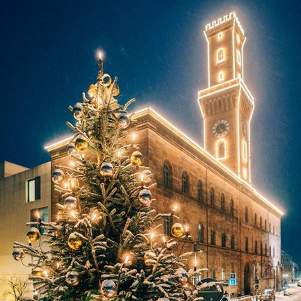 Das Fürther Rathaus leuchtet festlich, davor steht ein schneebedeckter Weihnachtsbaum am Kohlenmarkt