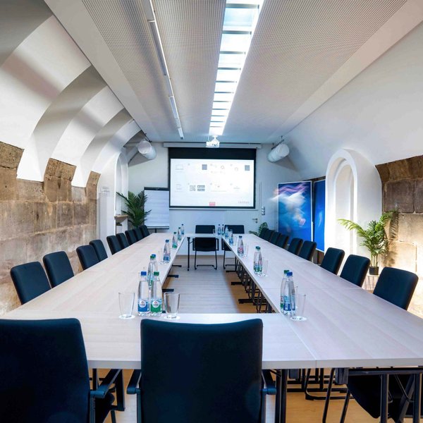 Kellergewölbe in Castros Bar mit rechteckig aufgestellten Tischen, Leinwand, Flipchart und Sandsteinwand