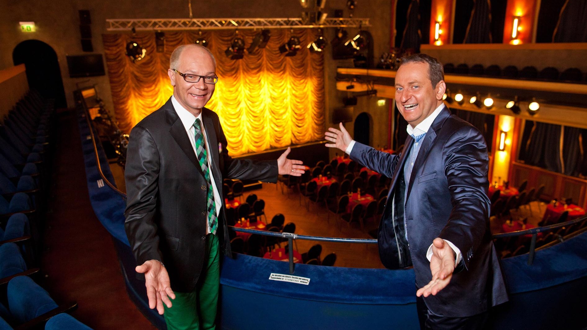 Volker Heißmann und Martin Rassau stehen auf der Empore in der Comödie Fürth, die Bühne ist bereit für die Vorstellung.