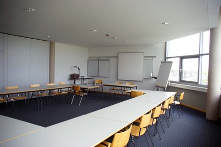 Moderner Tagungsraum im Complex Fürth mit Leinwand, Flipchart, U-förmigen Tischen und Teppichboden