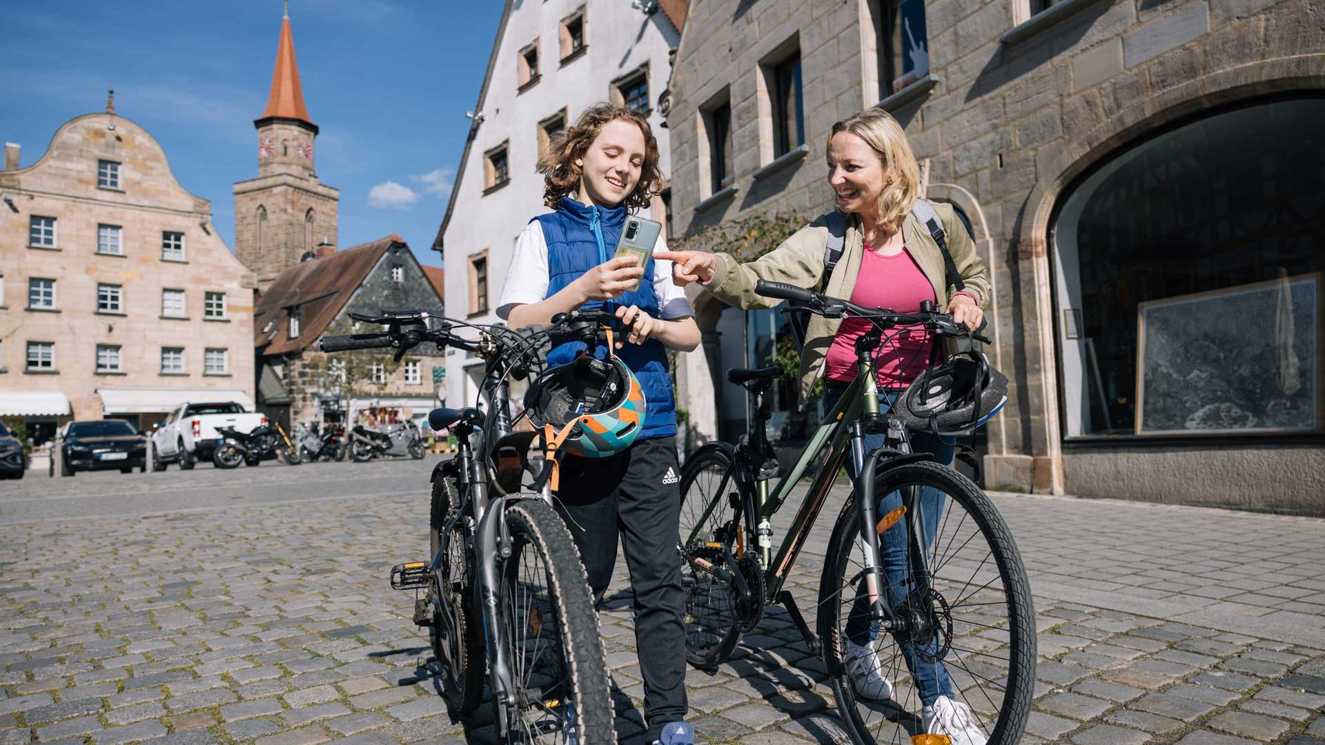 Frau und Junge schieben Fahrräder über den Grünen Markt, der Junge schaut aufs Handy