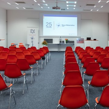 Langer Raum bei Neue Materialien Fürth mit Stuhlreihe, Teppichboden, Beamer und großer Leinwand