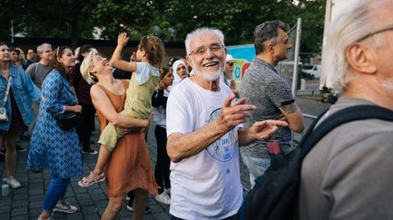 Fröhliche, tanzende Menschen aller Altersgruppen blicken lachend zur Bühne des New Orleans Festivals.