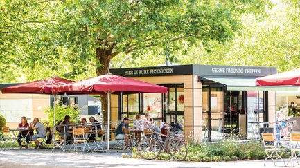 Essbereich auf dem Fürther Markt in Fürth mit roten Schirmen und überdachtem Innenbereich, Besucher genießen gekaufte Speisen