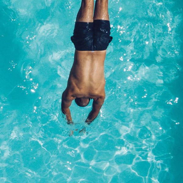 Eine Draufsicht zeigt einen Mann, der einen Stecher in das klare Wasser eines Schwimmbeckens macht