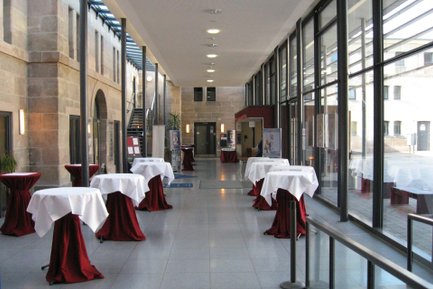 Eingangsbereich des Kulturforum Fürth mit großer Glasfassade, Sandsteingebäude dahinter und Stehtischen