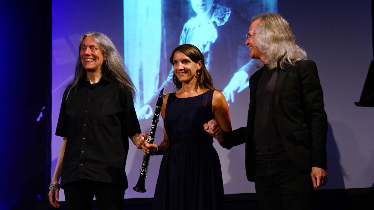 Drei Künstler halten sich nach ihrem Auftritt auf der Bühne vor der Projektion einer jungen Komponistin.