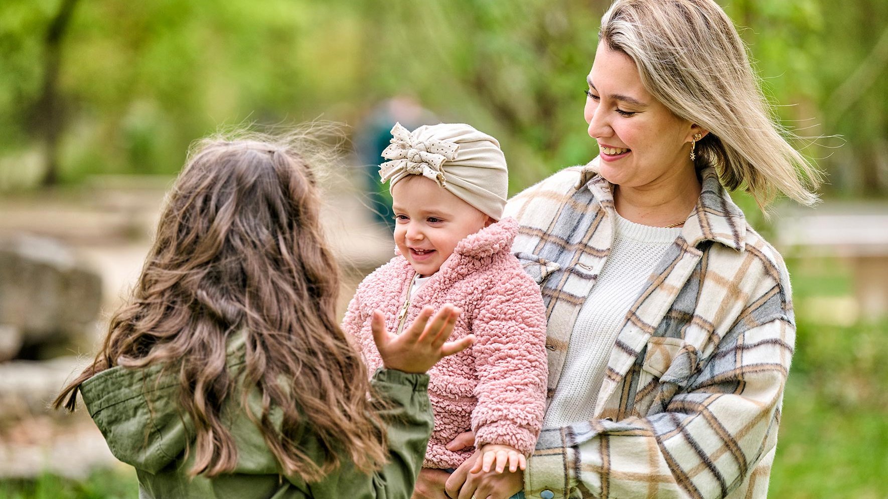 Eine junge Mutter und ihre Kinder auf einem Spielplatz in Fürth. Die Schwestern lachen zusammen im Grünen.