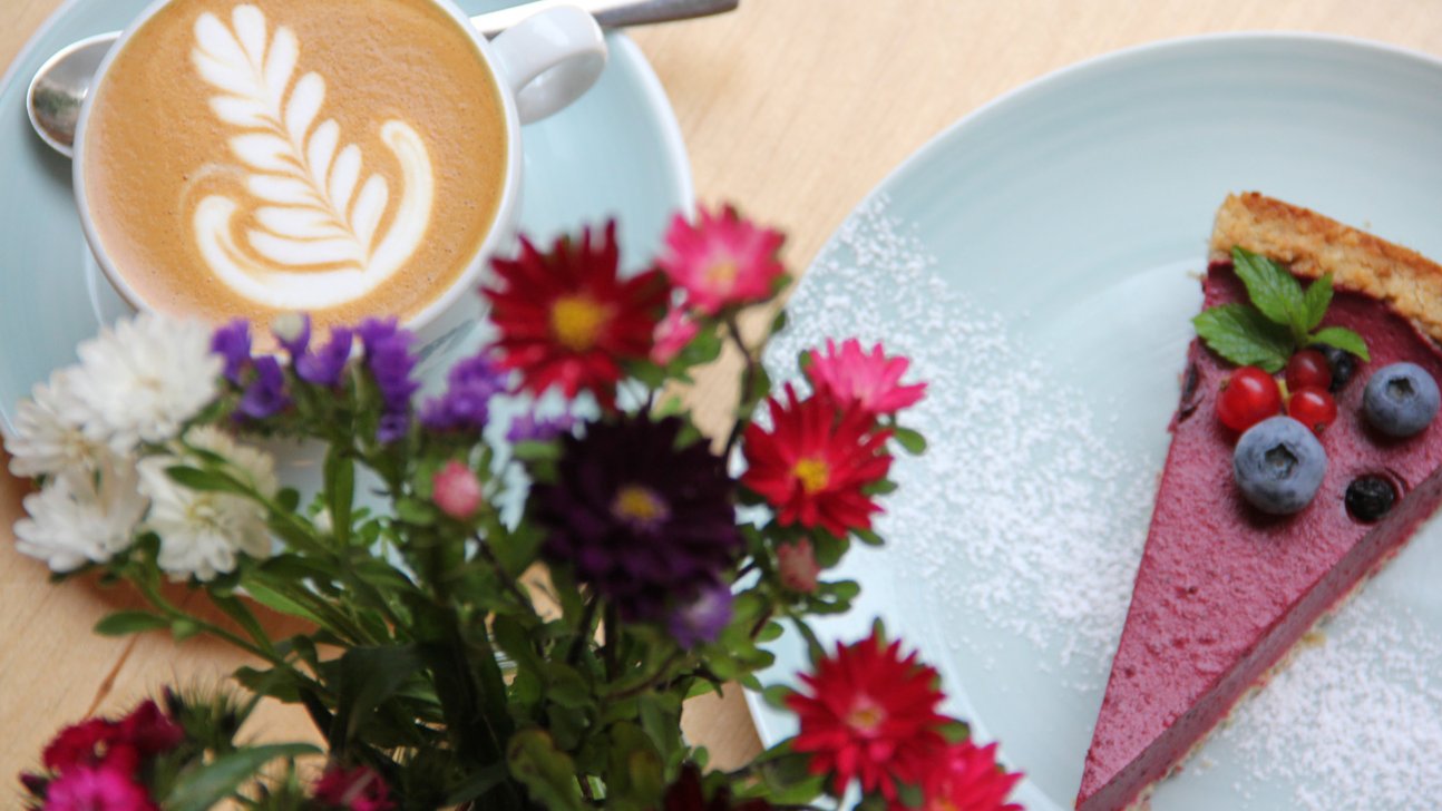Zwei kleine Teller mit Kuchenstück und verziertem Kaffee im stilvollen Kaffeesurium.