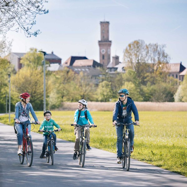 Eine vierköpfige Familie radelt auf einem asphaltierten Weg im Grünen, im Hintergrund der Fürther Rathausturm.