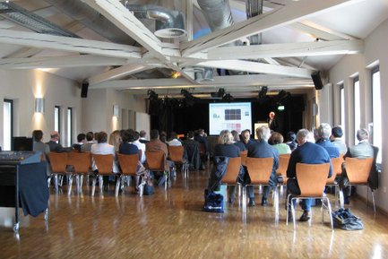 Blick von hinten auf Stuhlreihen im Kulturforum Fürth mit Vortrag auf Bühne und Leinwand