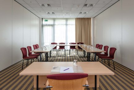 Kleiner Tagungsraum mit Tischen in U-Form, vorn ein Tisch mit Block, Stift und Glas für Präsentationen