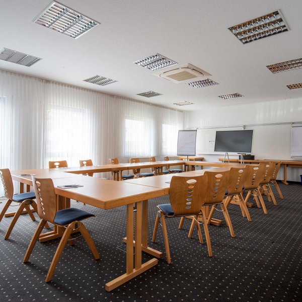 Heller Tagungsraum im Landhotel Seerose mit Holztischen, Stühlen, großem Bildschirm und Tischen mit Block und Stift