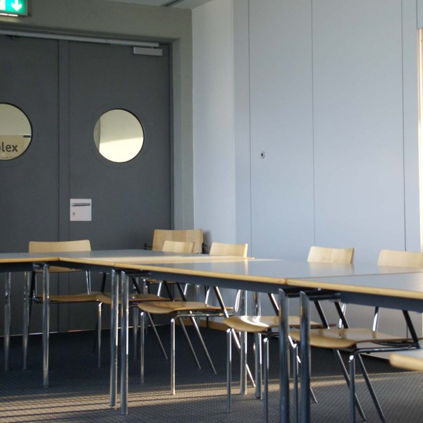 Stuhlreihe im Raum des complex Fürth mit Tür und rundem Fenster im Hintergrund