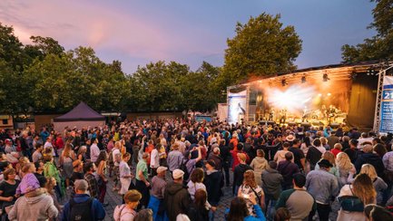 Fröhliche, tanzende Menschen schauen zur Bühne, auf der eine Band beim New Orleans Festival spielt.