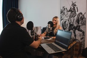 Zwei Podcaster der Tourist-Information Fürth sitzen am Tisch vor Mikrofonen und nehmen eine Folge auf