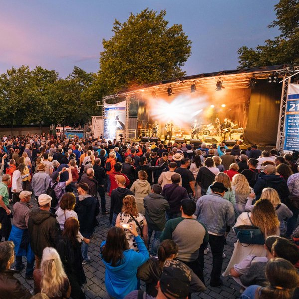 Fröhliche, tanzende Menschen schauen zur Bühne, auf der eine Band beim New Orleans Festival spielt.